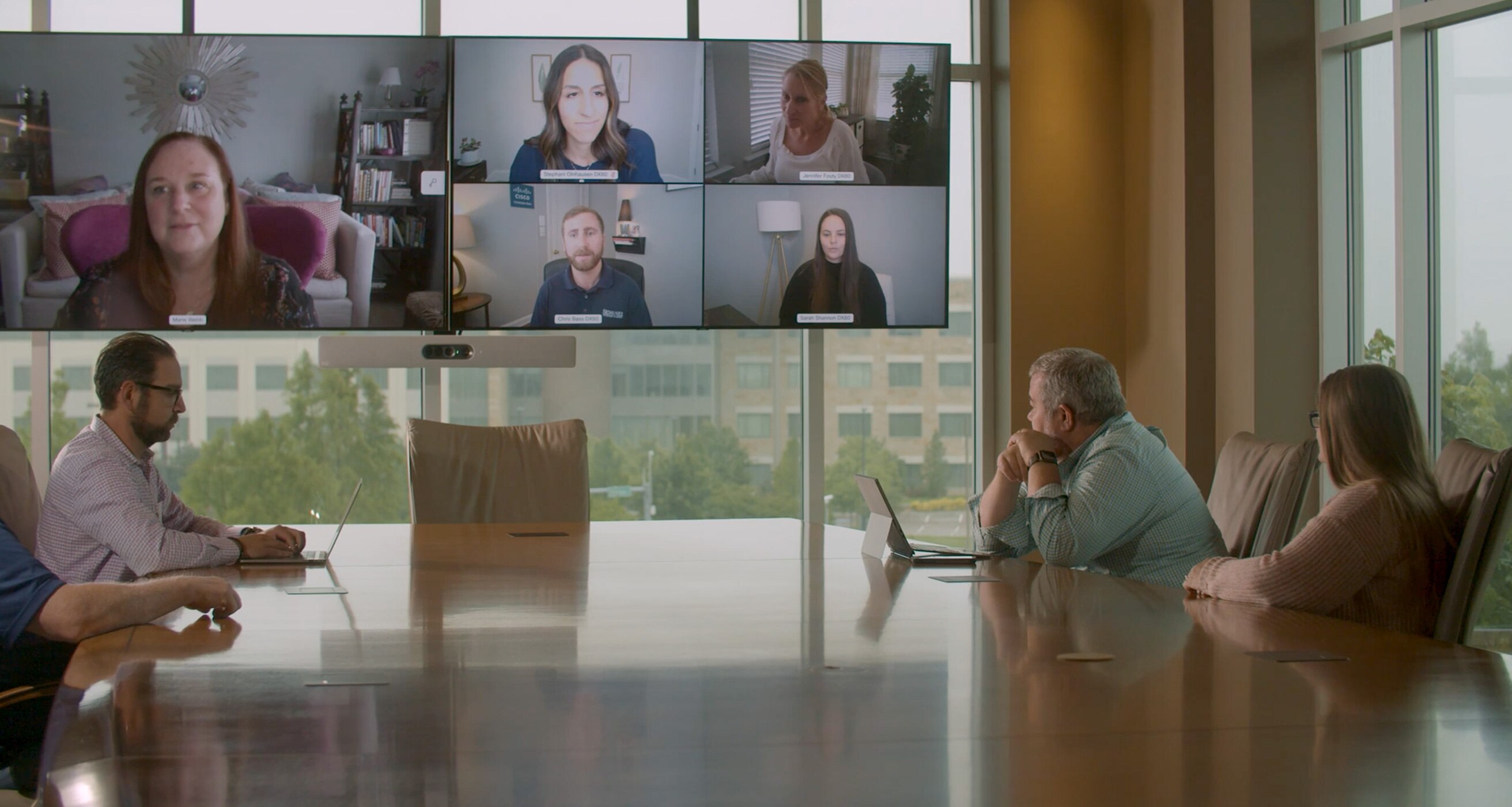 Colleagues in a conference room collaborate with several other colleagues via a video meeting.